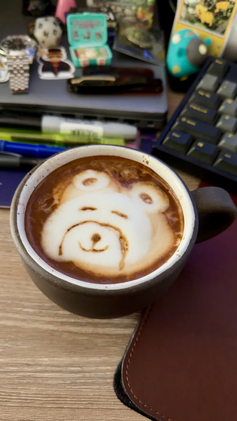 A bear face drawn into the foam of a latte in a dark brown cup.