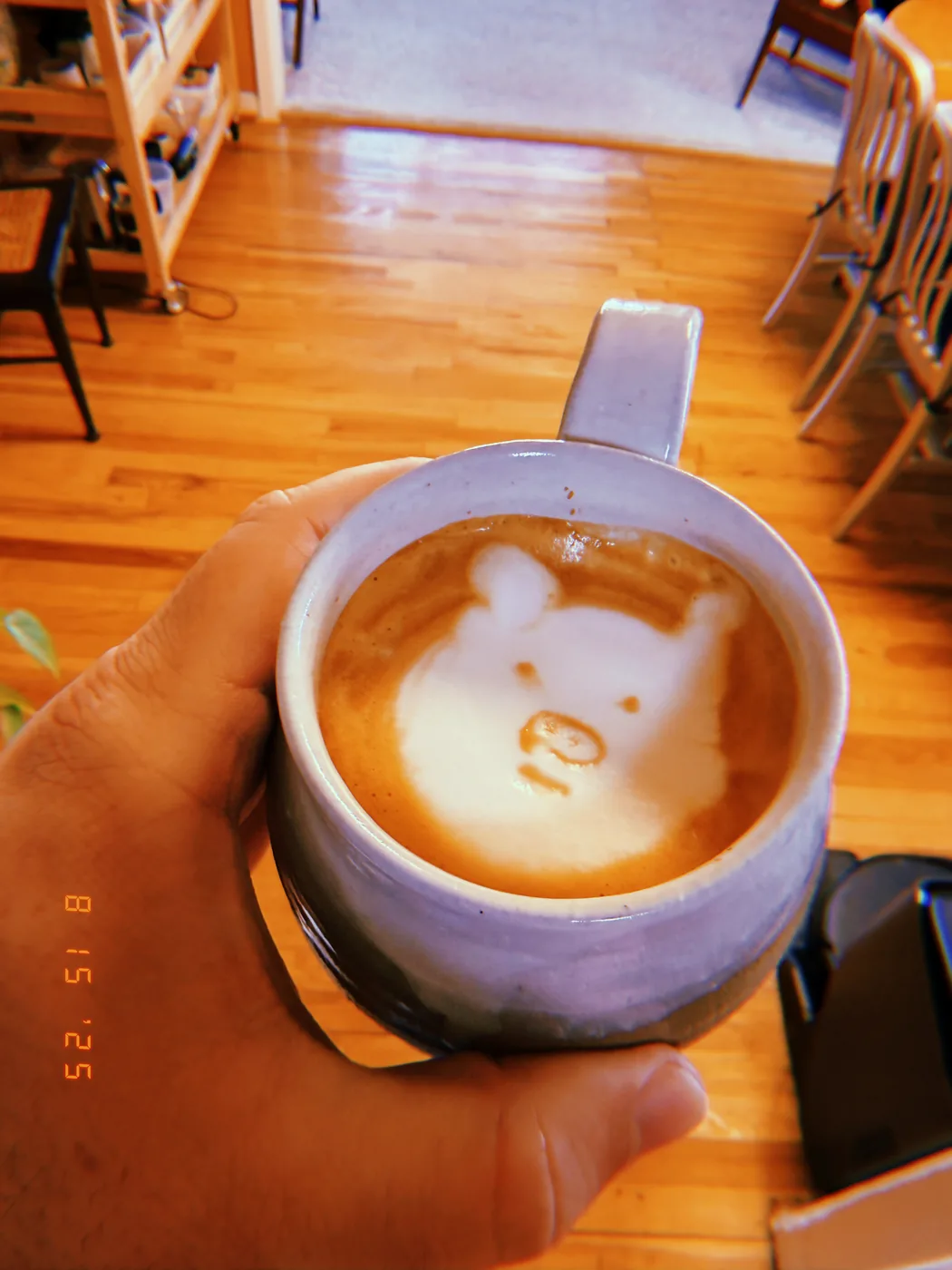 A hand holding a white cup with a bear face in its latte foam.