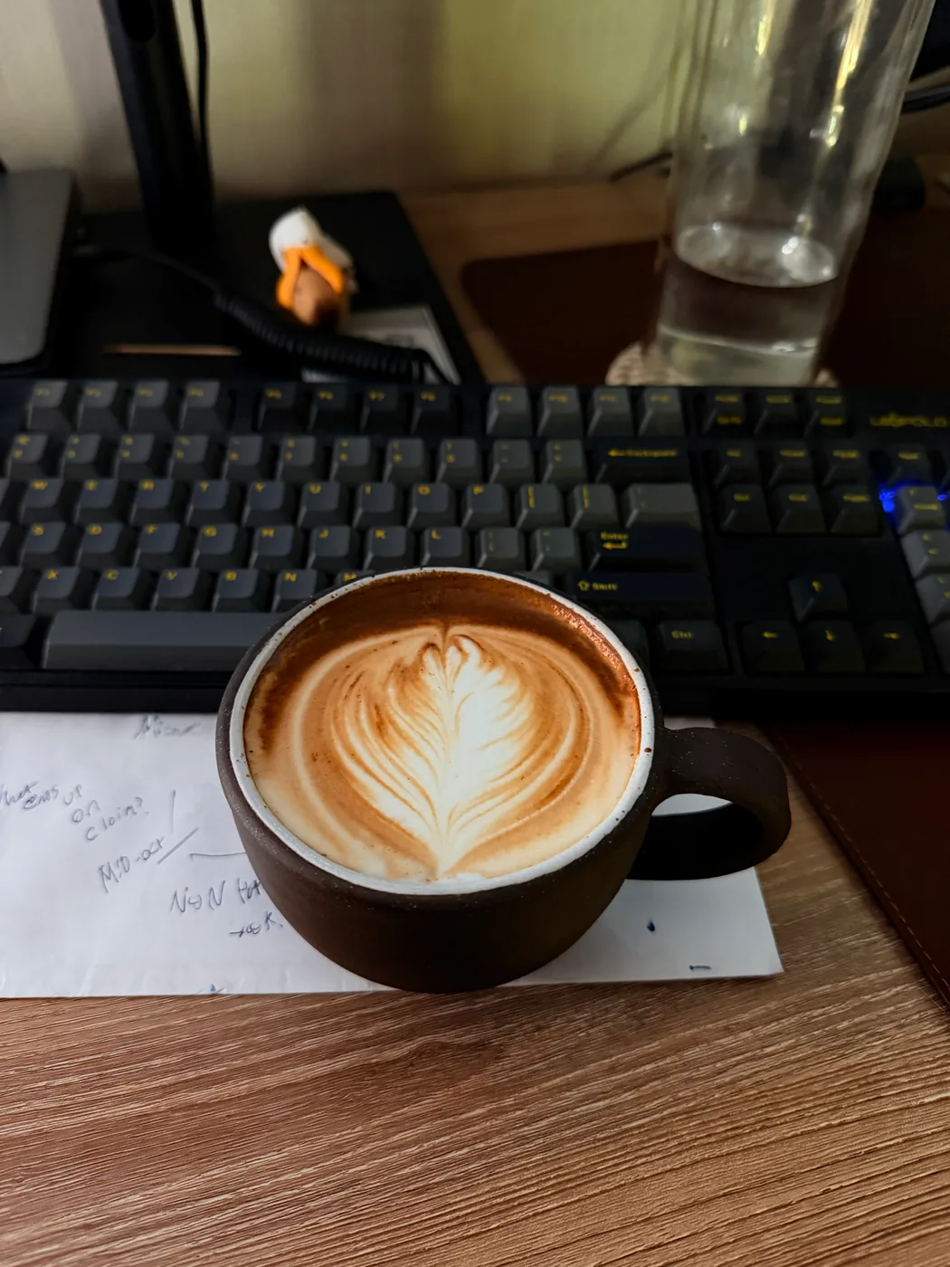 A heart shaped leaf pattern in a brown ceramic latte cup on a desk.