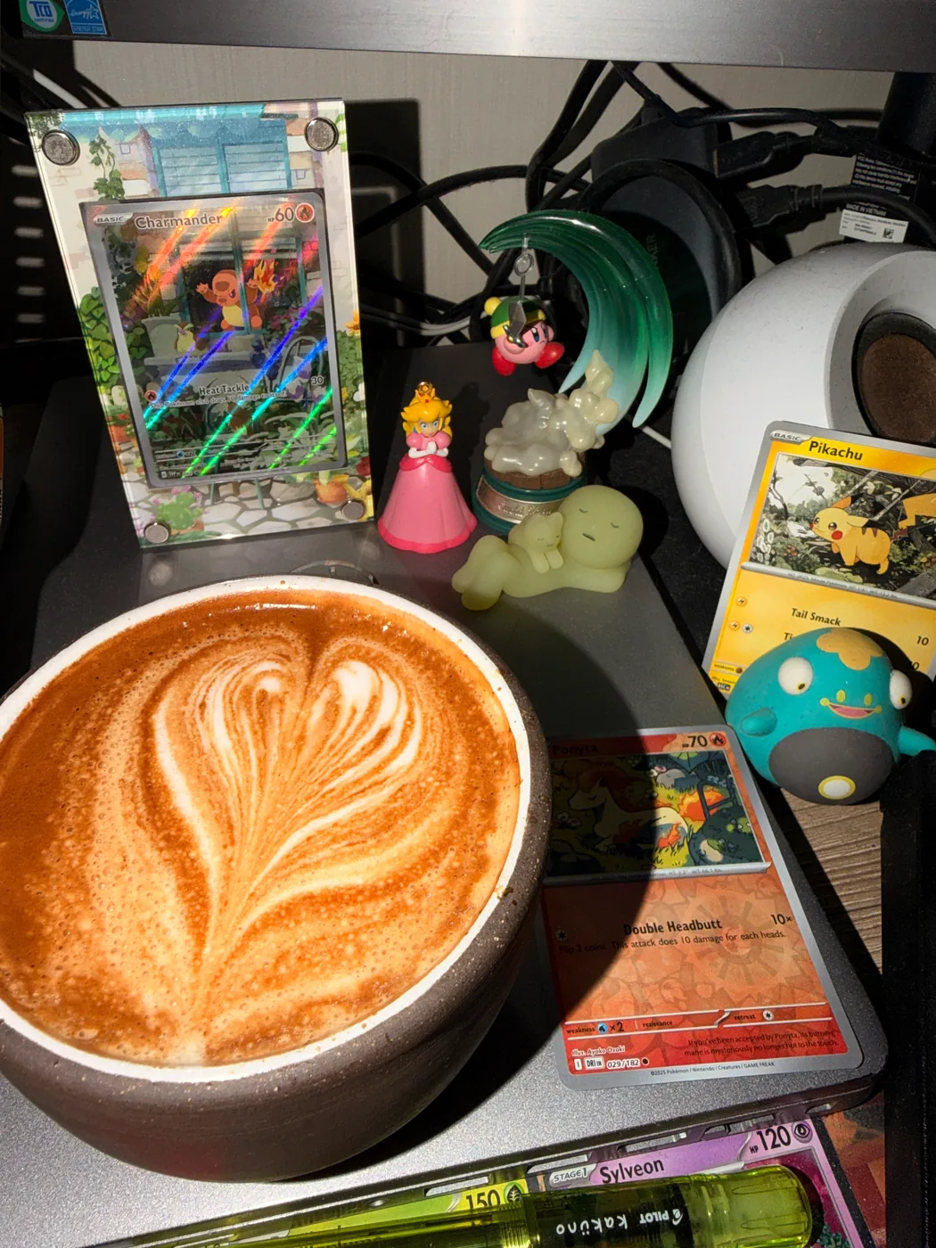 A layered leaf pattern poured into a dark latte with Pokémon cards and figures nearby.