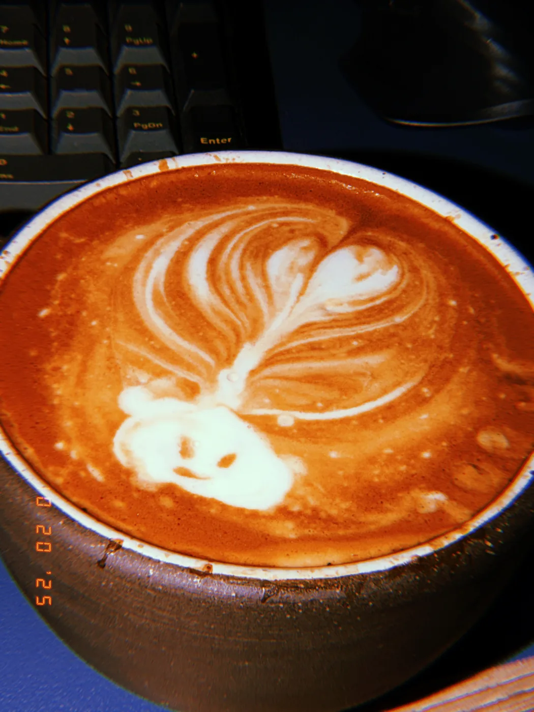 A close view of a layered latte art leaf that ends in a tiny smiling face.