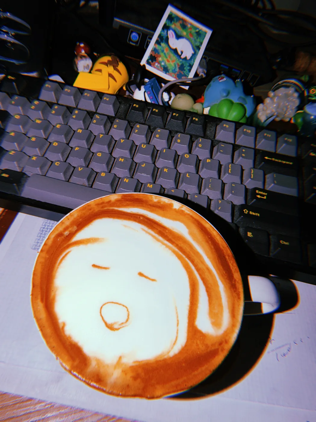 A simple sleepy face drawn in latte foam in a white cup beside a keyboard.