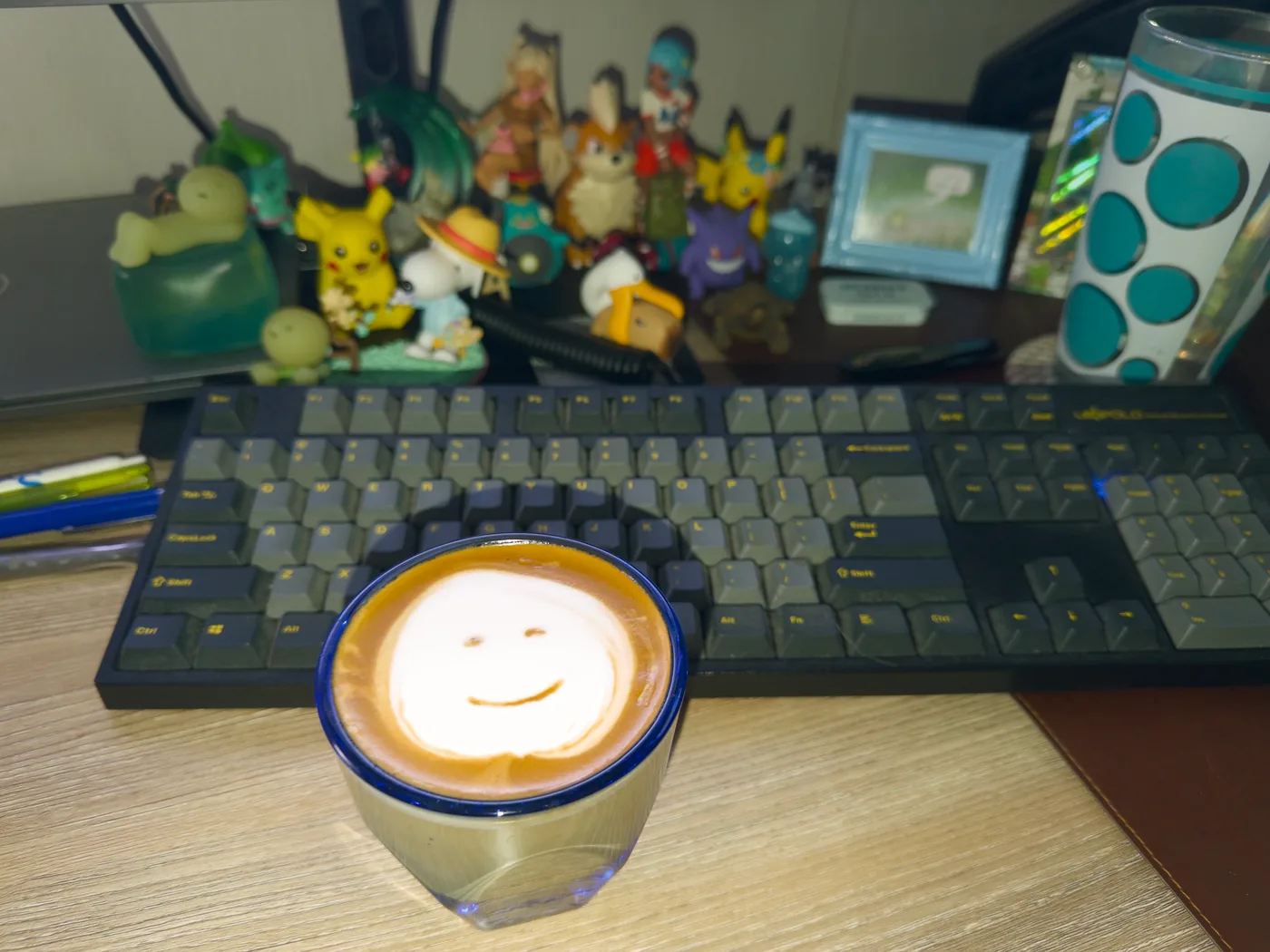 A smiling face in latte foam in a blue rimmed cup in front of a keyboard and figures.