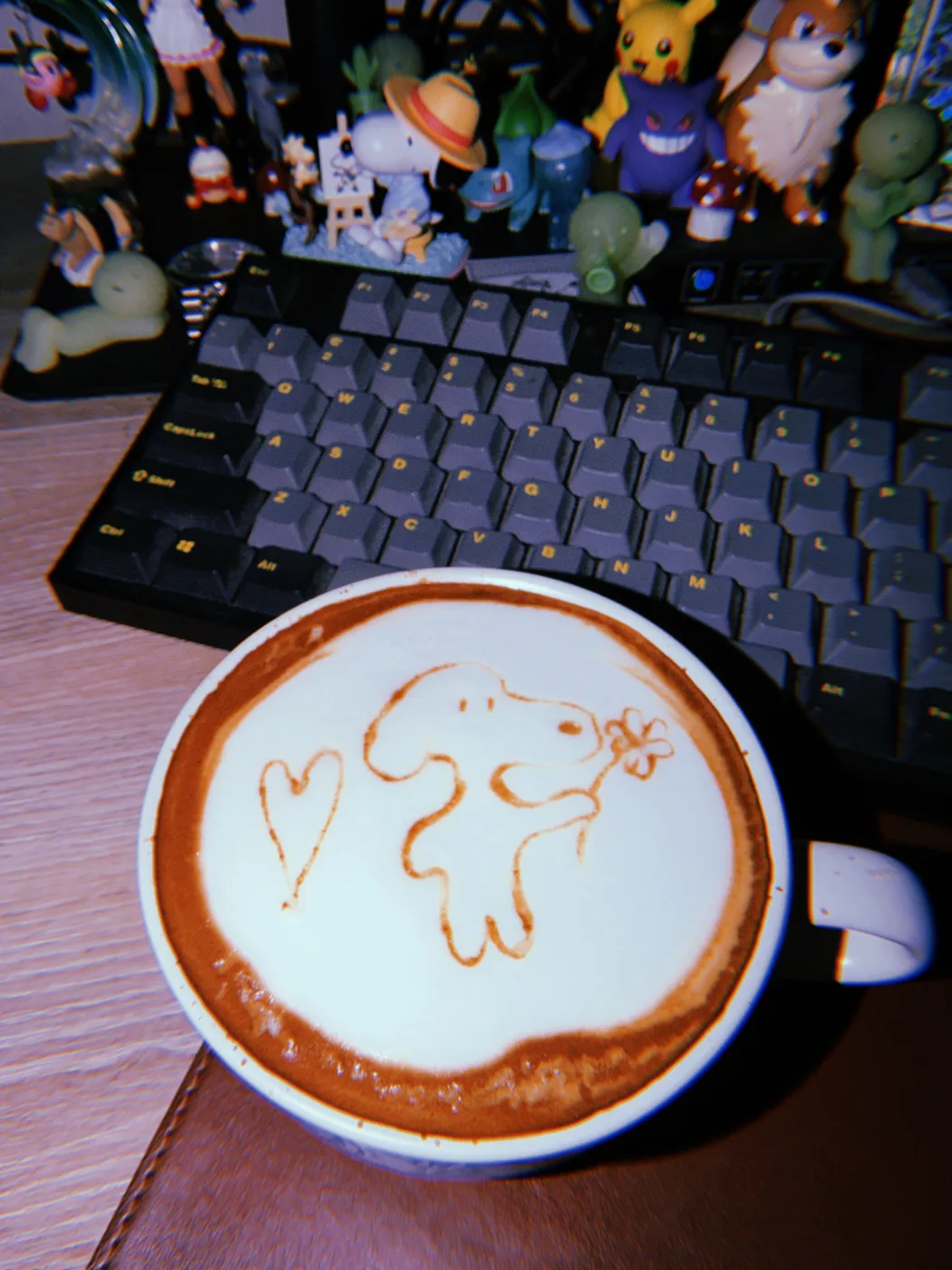 A Snoopy drawing and a heart in latte foam, with Pokémon figures behind the cup.