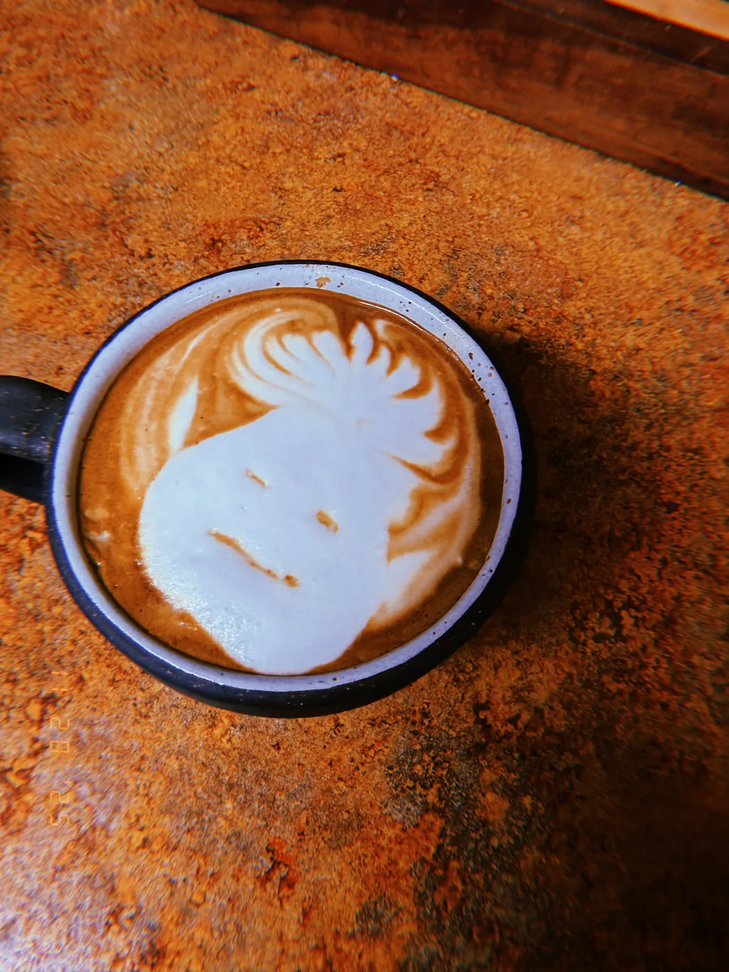 A softly smiling face made from latte foam in a cup on an orange tabletop.